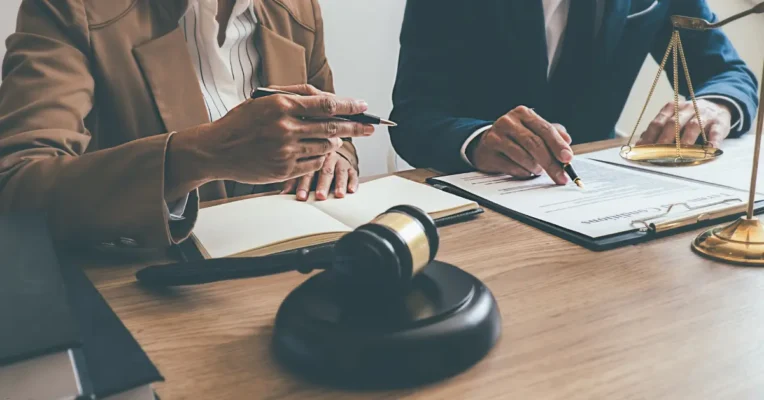 Two probate lawyers discussing terms of a contract with scales of justice and a gavel on the desk