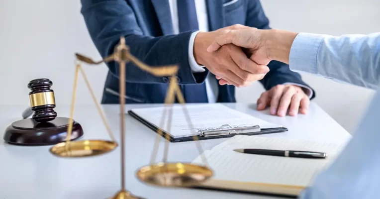 estate lawyer and client shaking hands over a desk with legal documents, scales of justice, and a gavel.