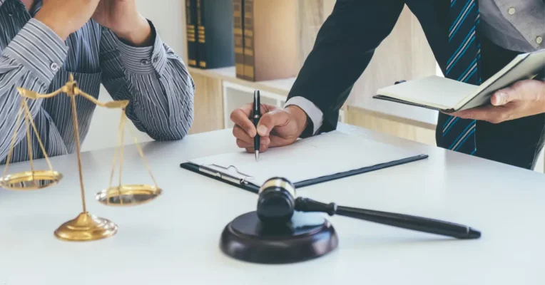 Probate lawyer pointing to a document for a client to sign, with scales of justice and a gavel nearby.