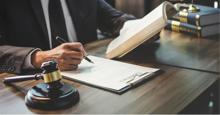 Estate lawyer reviewing and signing a contract with an open book and gavel on the desk