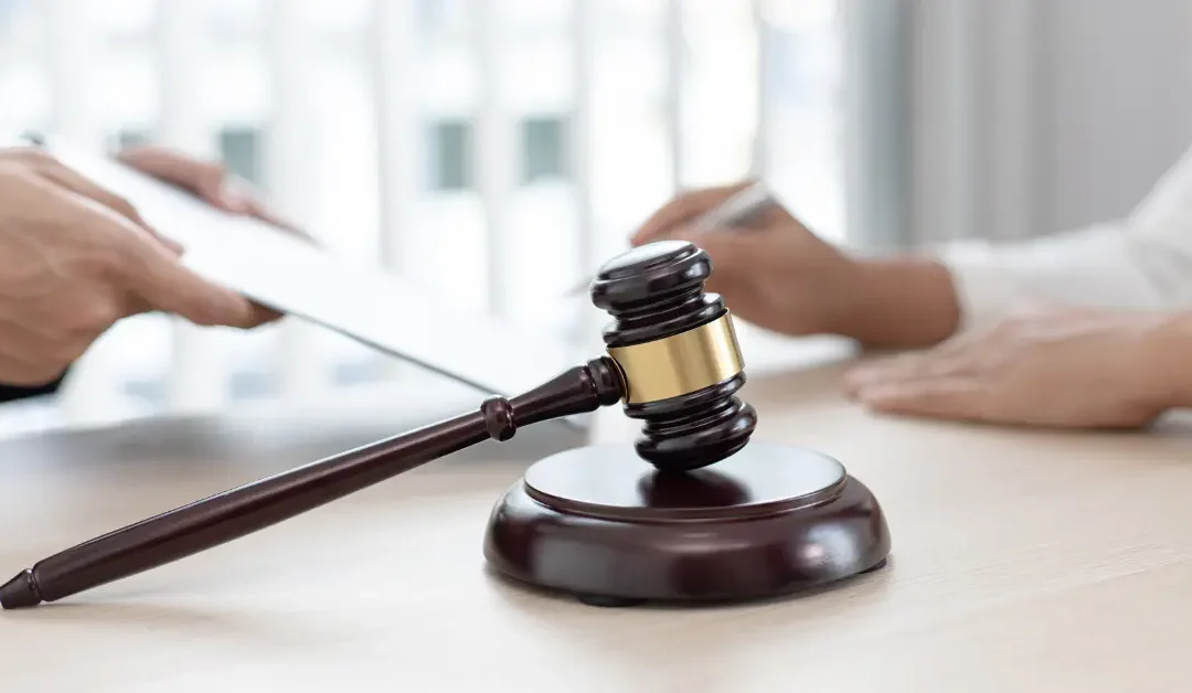 Close-up of a gavel in focus as a probate lawyer hands a document to a client in the background.