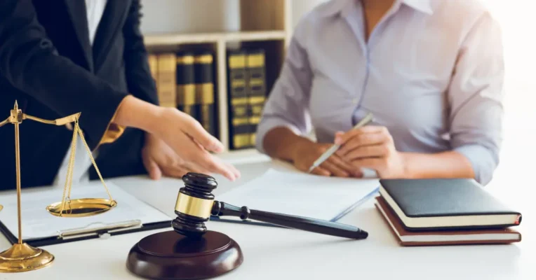 Probate lawyer pointing to a document while a client reviews paperwork, with a gavel and scales on the table.