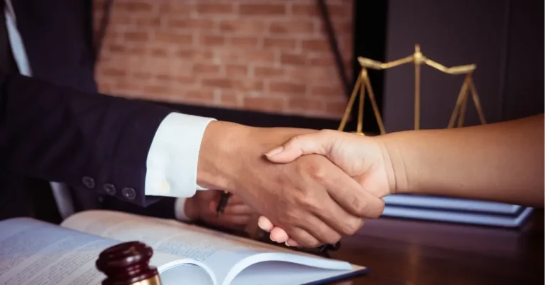 estate lawyer and client shaking hands over an open book, with scales of justice in the background.