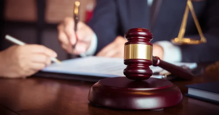 Close-up of a gavel in front of two estate lawyers signing documents