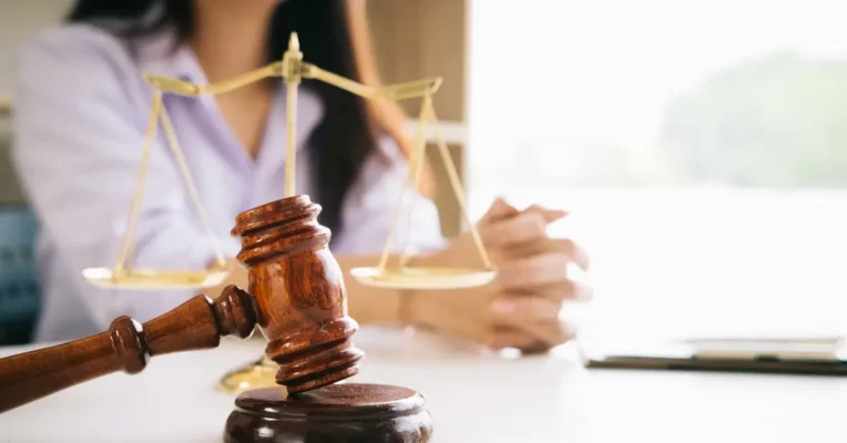 Close-up of a gavel and scales of justice on a trust lawyer’s desk, with hands folded in the background