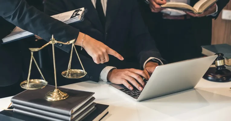 Attorney for wills working on a laptop while referencing legal books and documents with scales of justice nearby